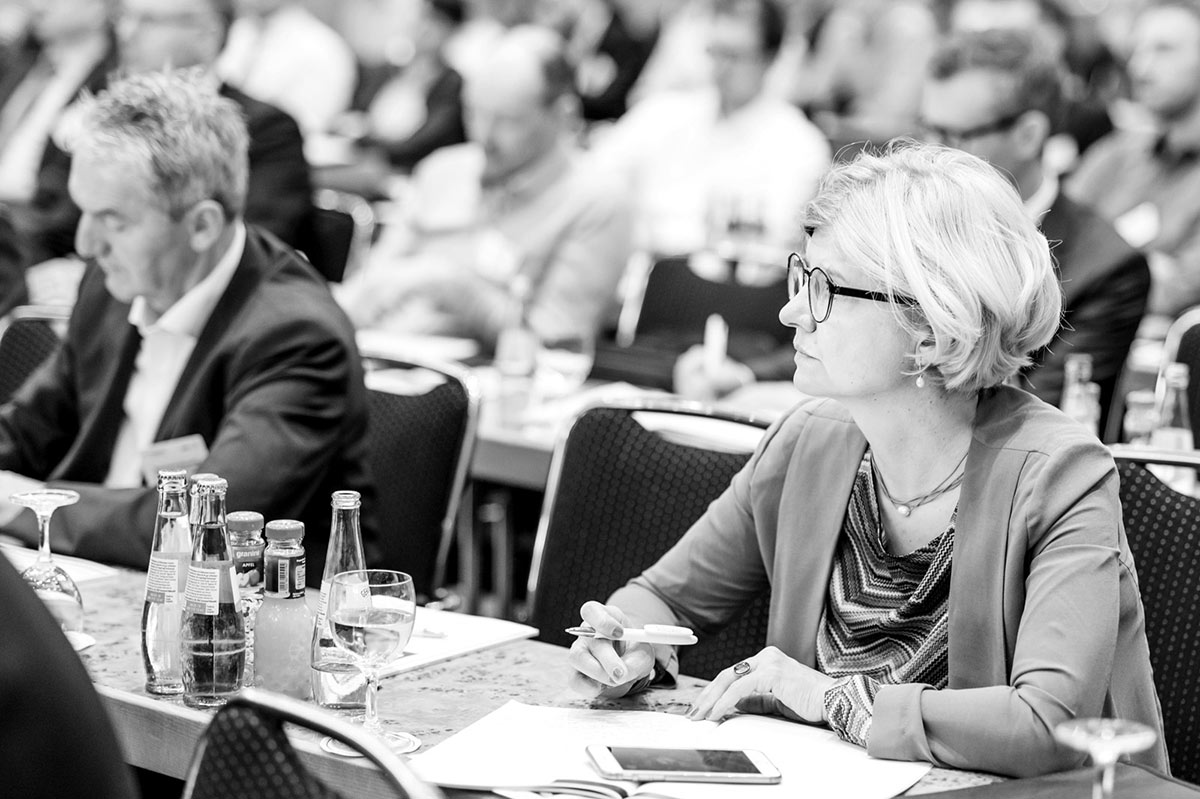 Konferenzteilnehmende sitzen im Plenum und verfolgt einen Vortrag. 
